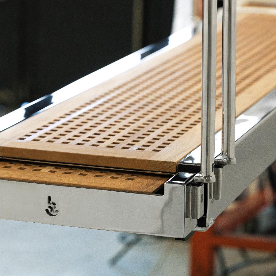 Dettaglio del logo su passerella automatica idraulica a scomparsa con carabottino in teak e struttura in acciaio lucido per barche a motore